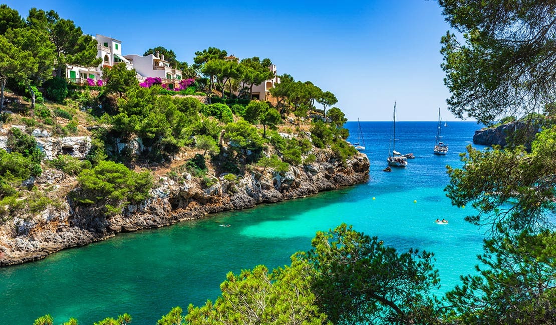 Blick auf eine Bucht mit blauem Wasser und Botten in Ibiza