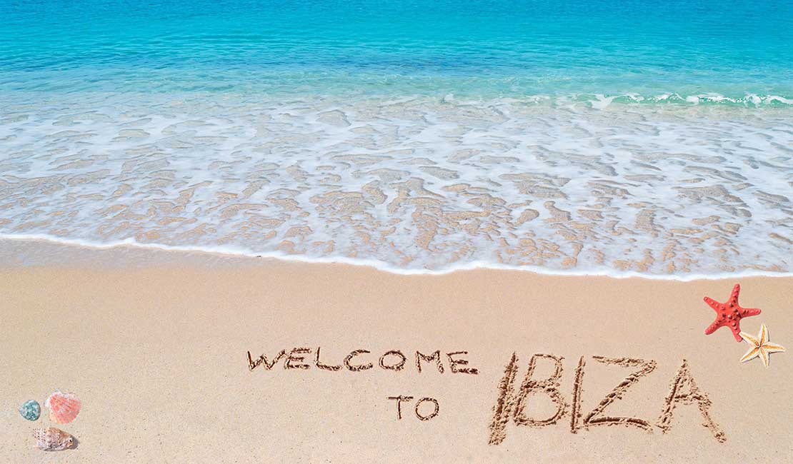 Blick auf blaues Wasser am Strand mit Schriftzug 'Welcome to Ibiza' im Sand